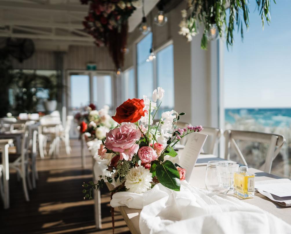 Coast Port Beach wedding reception set up with colourful flowers in front of a window and the beach in the background 