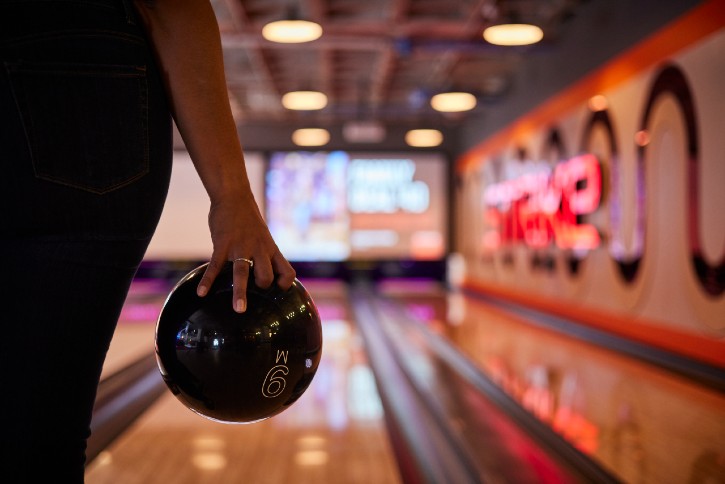 An arm holding a bowling ball and about to bowl down the lane at Strike 