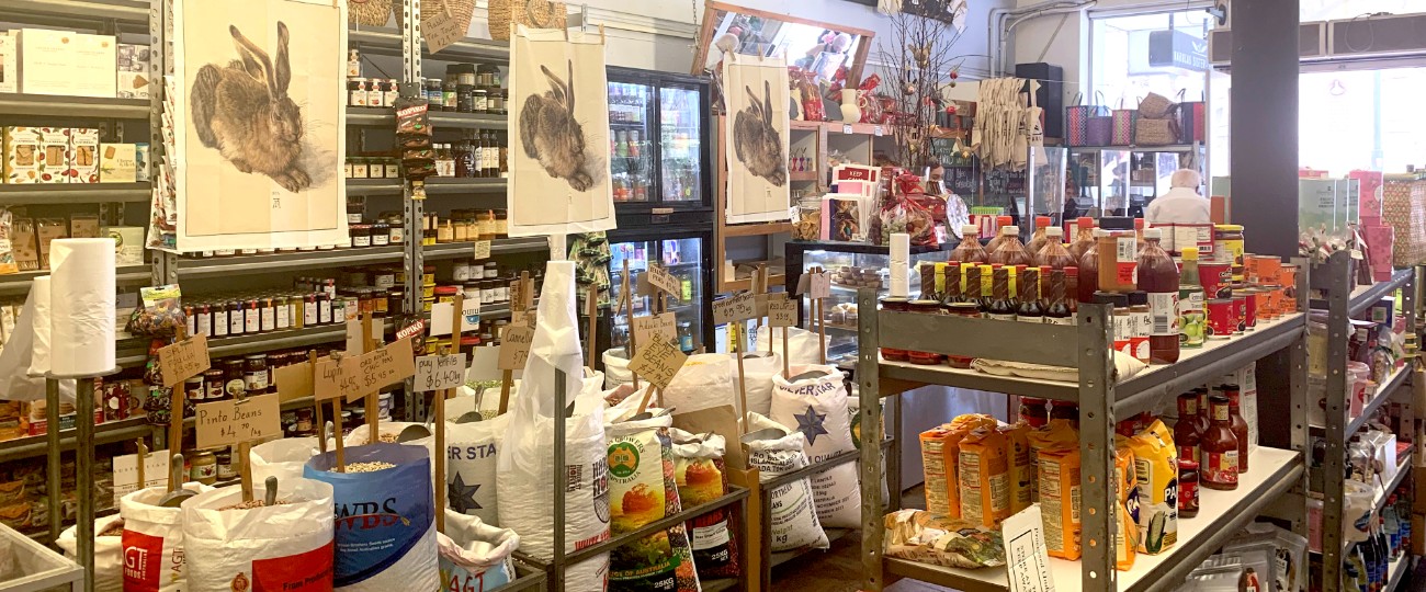 Shop interior with shelves of bulk foods, jars and colourful packets and hanging tea towels with pictures of rabbits