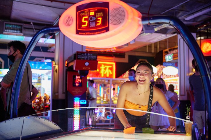 smiling person plays colourful game in neon lit retro arcade