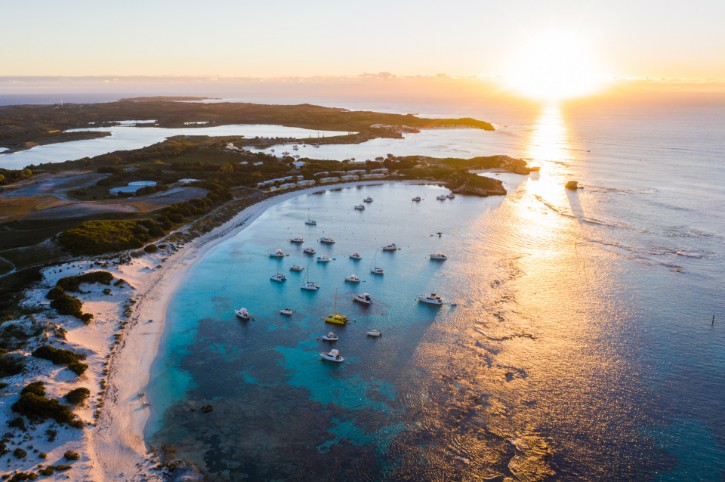 aerial view across turquoise bay with setting sunlight glistening across water