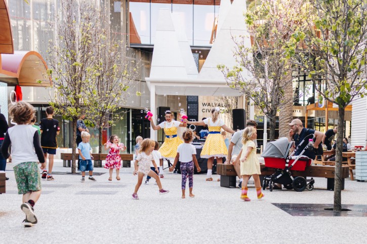 children playing with bubbles in a vibrant, tree lined square, with smiling entertainers dressed in yellow