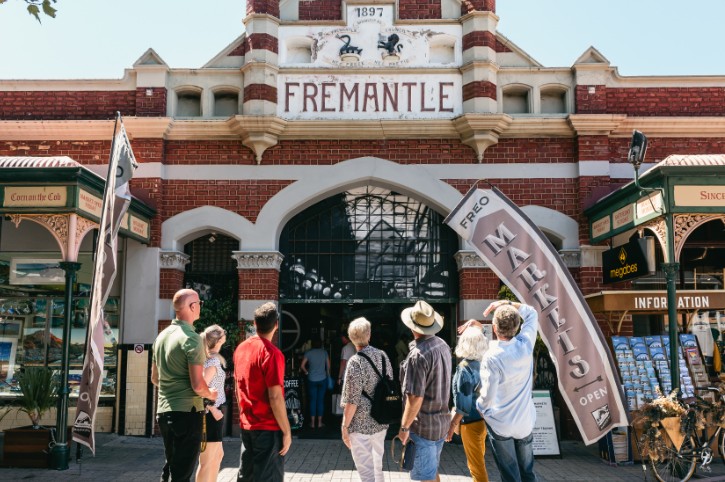 group of people stand outside fremantle markets, looking up at historic building