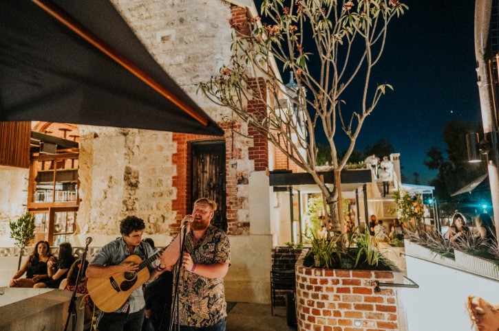 two musicians play in a restaurant with exposed brick walls and trees