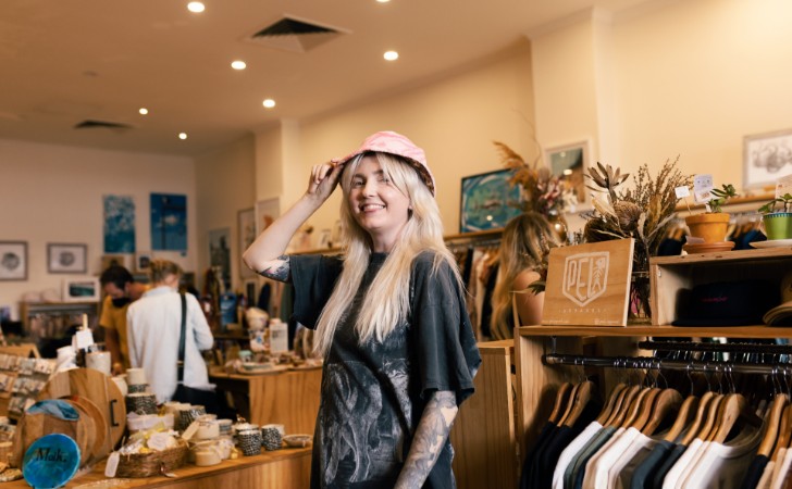 person in a fashion and gift store wears pink hat and smiles cheekily at camera