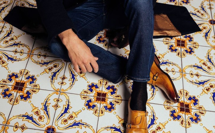 well dressed person sits on ornate tiled floor wearing stylish leather shoes, trousers and jacket