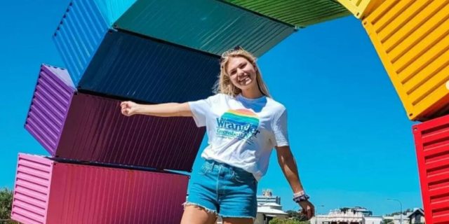 Person poses in front of Marcus Canning's 'Rainbow', known as 'Containbow' - sculpture of colourful shipping containers