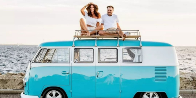 Couple sits on top of turquoise van in front of beach
