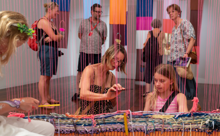 family weaves neon pink threads on an interactive art exhibition