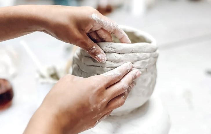 Two hands mould a piece of white pottery into shape.