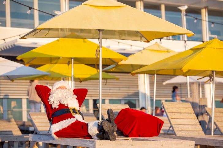 Santa reclining under a beach umbrella with a full bag of presents next to him.