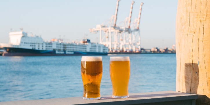 Two beers on a bench overlooking a port with a ship in the background.