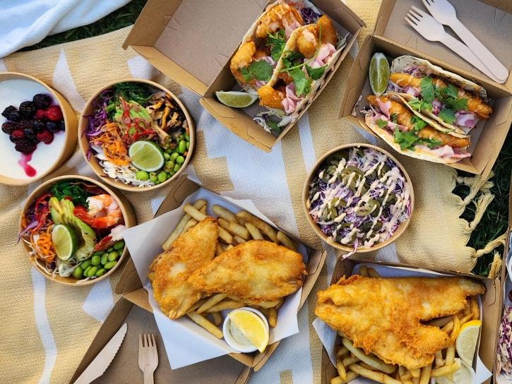 Fish and chips, poke bowls, and fish tacos spread out on a beach towel.