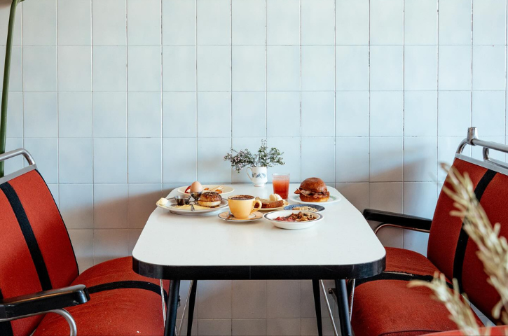 an empty table laid out with breakfast with red chairs and a tile wall 