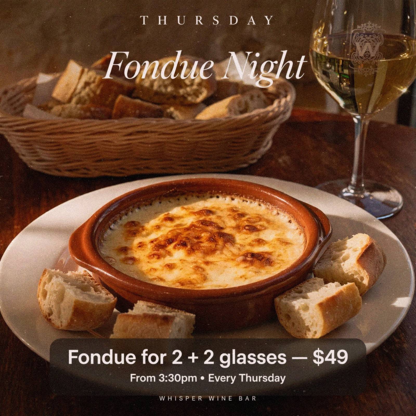 a fondue dish with cut bread and a wine glass in the background