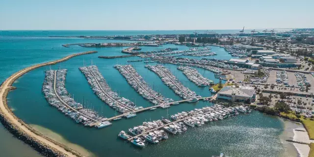 aerial photo of rows of boats parked along jetties at the sailing club. boats are separated from the ocean by a large curving limestone groyne. 