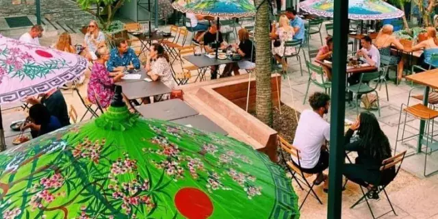 looking down through colourful umbrellas in lush courtyard where people are chatting and dining