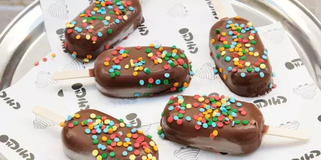 A silver tray with five icecream popsicles on it covered in milk chocolate and sprinkles.