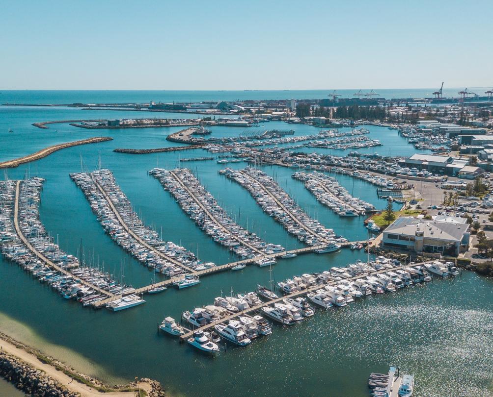 aerial photo of rows of boats parked along jetties at the sailing club. boats are separated from the ocean by a large curving limestone groyne. 