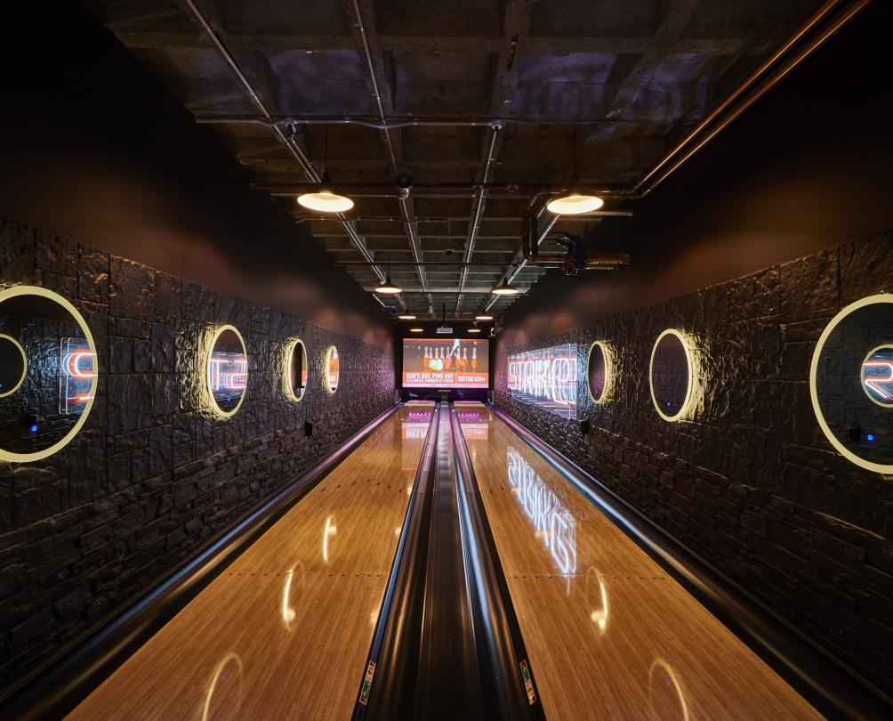 Strike bowling, two polished wood lanes with large circular feature lights along dark colours walls