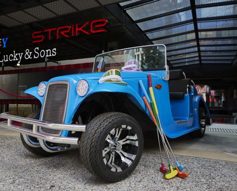 Blue vintage car parked in front of FunLab with colour golf putters leaning against it 