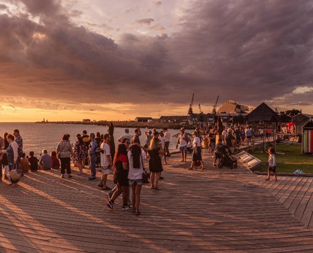 Sunset over Sculpture at Bathers exhibition 2020 crowd gathered at Bathers Beach at sunset for Sculpture at Bathers with Norfolk pine tree in the background