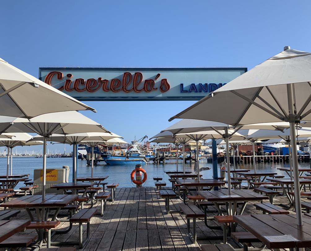 white umbrellas and wooden tables on waterfront deck in front of Cicerellos' sign