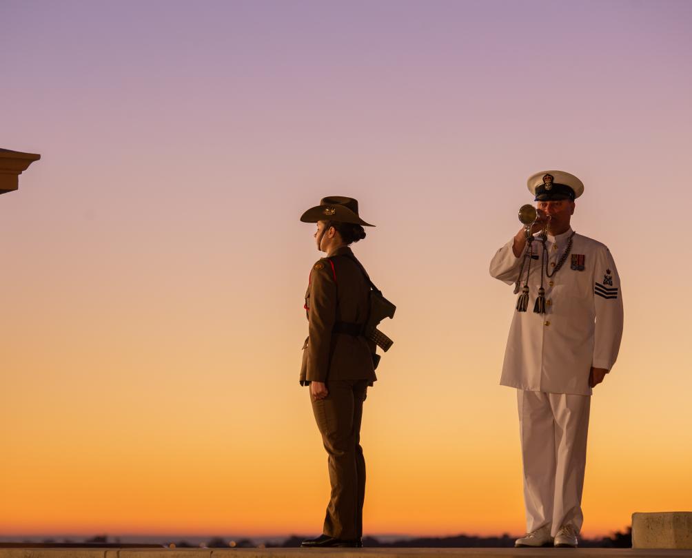 two service people standing in uniform at monument with sunrise