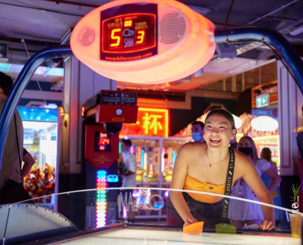 smiling person plays colourful game in neon lit retro arcade