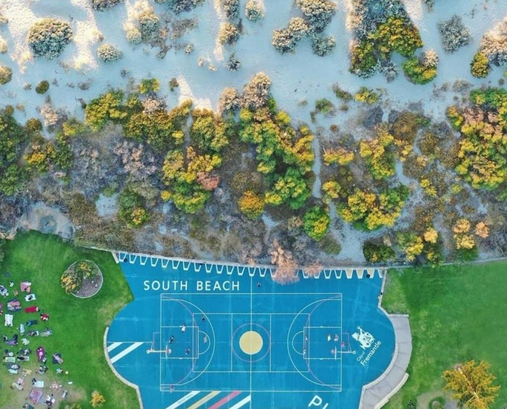 aerial shot of basketball court next to white beach with turquoise ocean