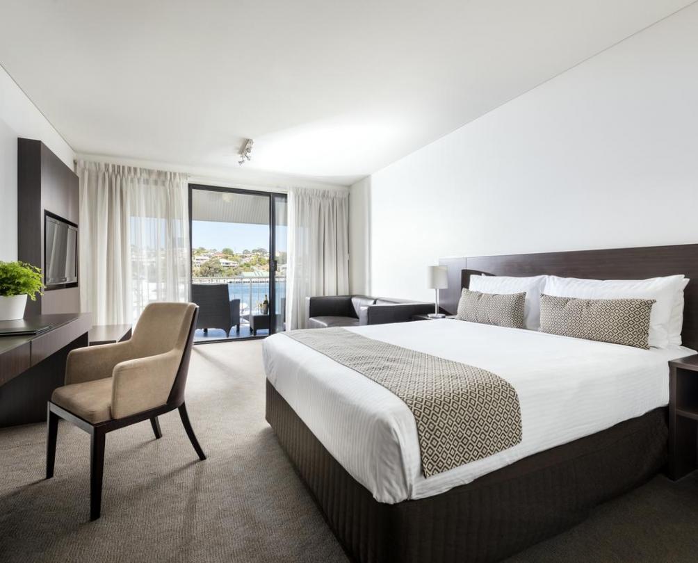 Interior of hotel room - large bed with side table, chair and sliding doors with view out to Swan River 