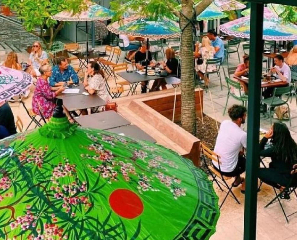 looking down through colourful umbrellas in lush courtyard where people are chatting and dining