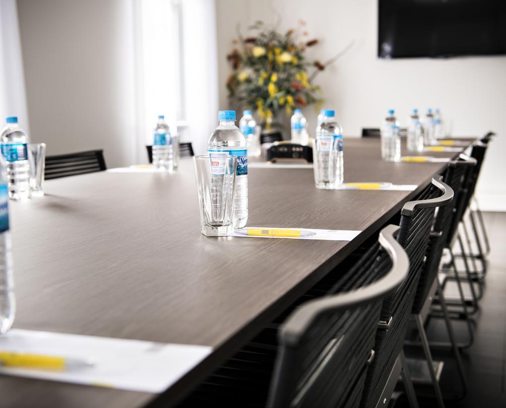 Board room table surrounded with office chairs and set with pens, paper and bottle water