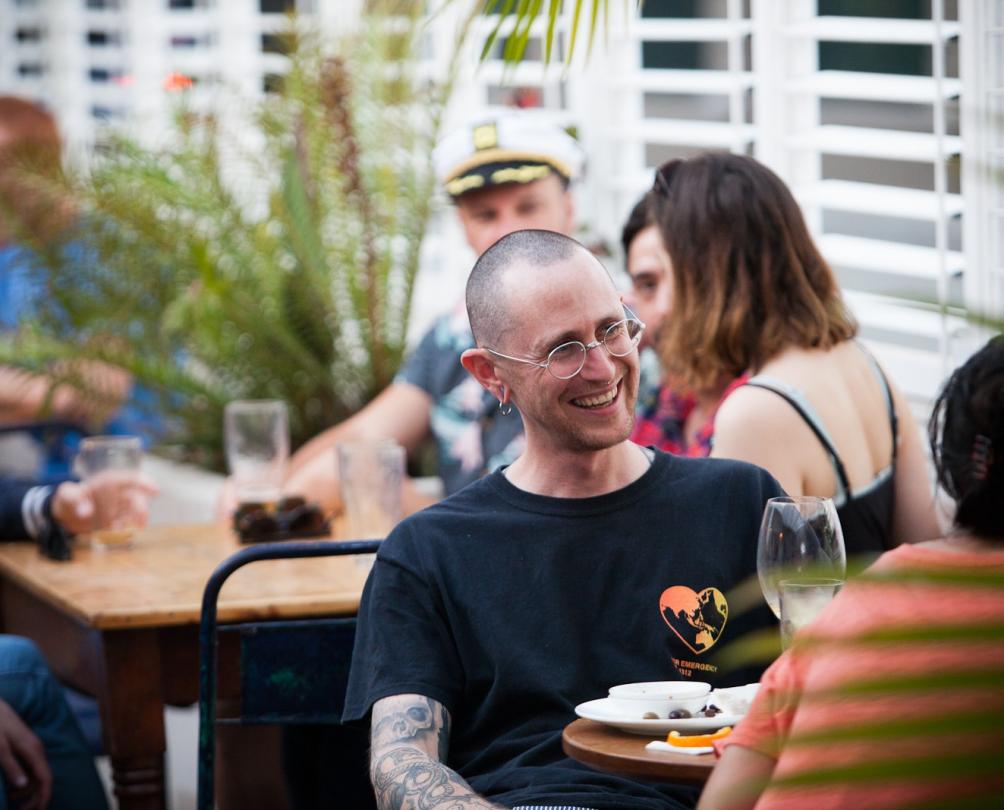 person smiling and enjoying casual food and drink with friends at a small al fresco bar