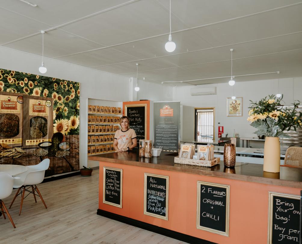 Branka's Crackers store interior - pink counter, feature wall painted with sunflowers, Branka standing behind the counter