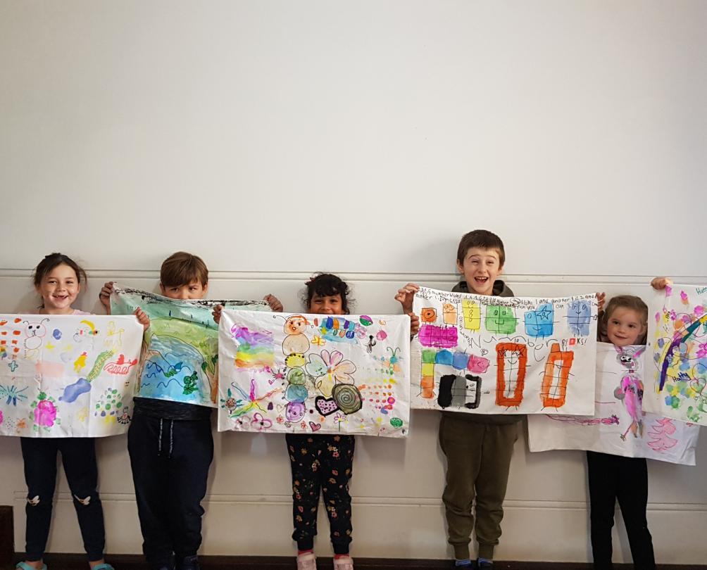 Row of young children holding up their artwork at Fremantle Arts Centre kids classes designing and printing on pillowcases