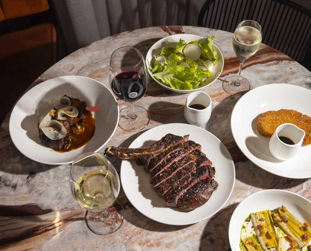 Plates of food displayed on table at Cassia with glass of wine 