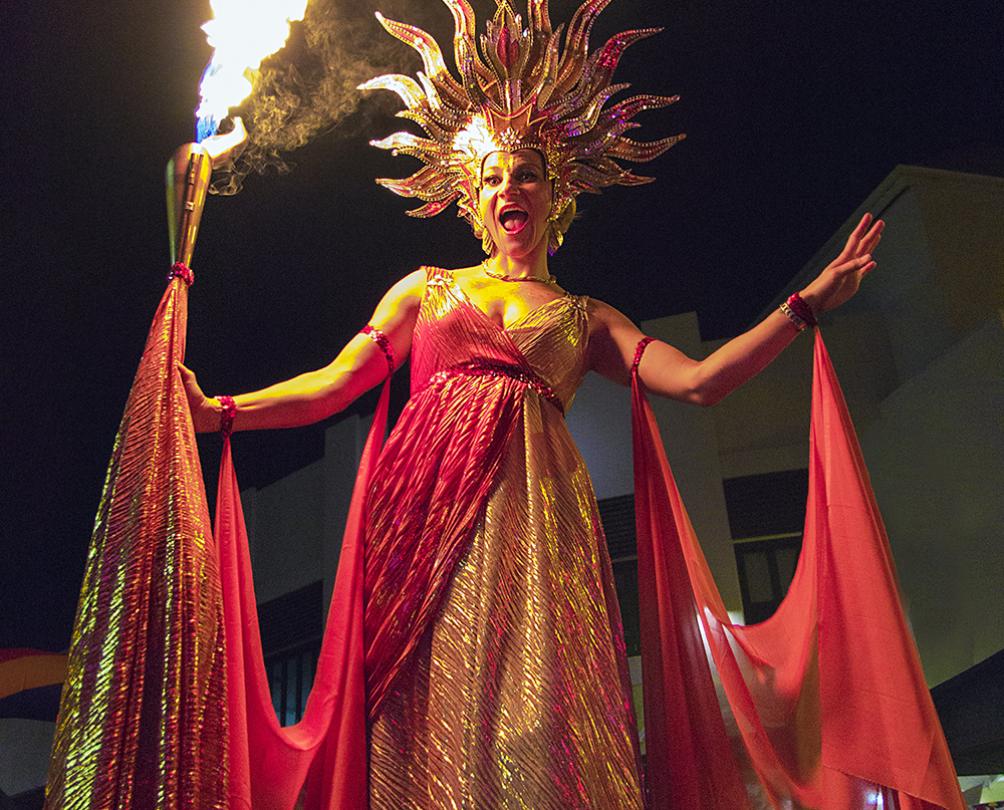 A stiltwalker in a red and and gold dress plays with fire.