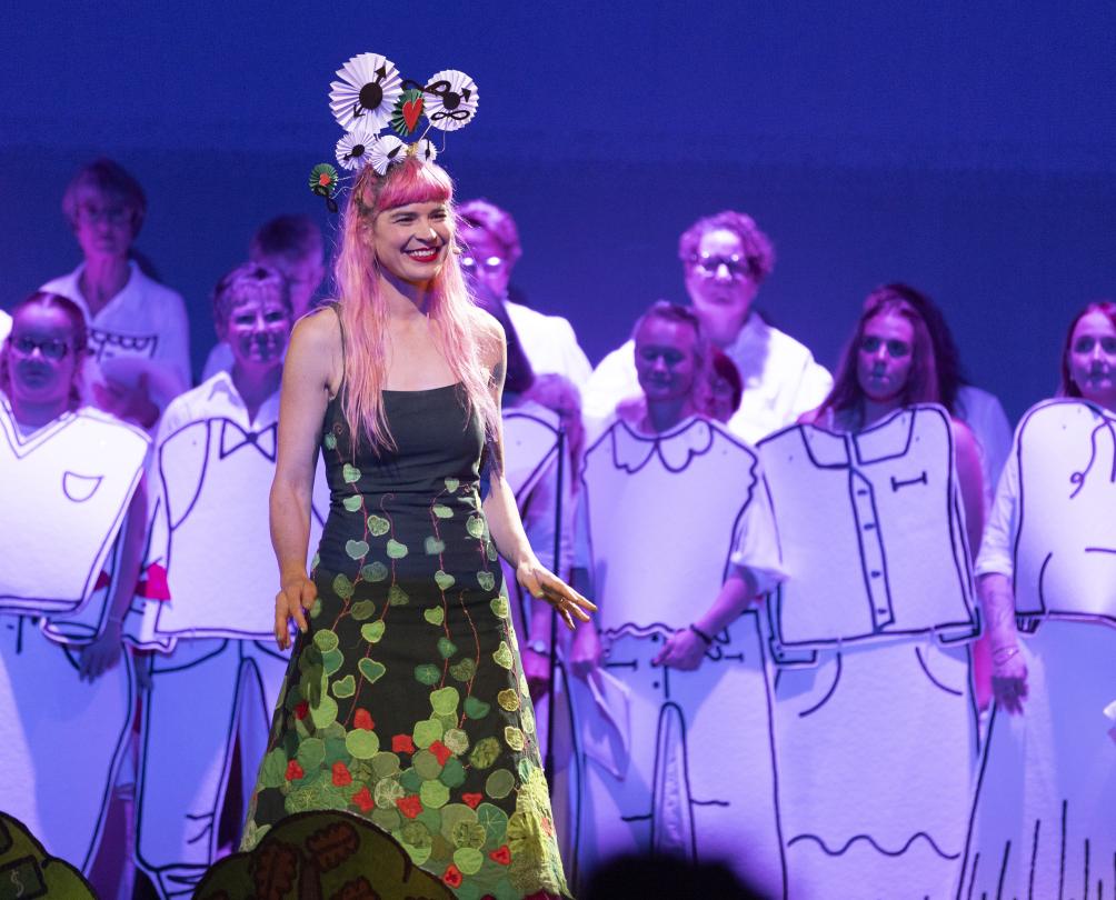 A woman in a green dress performs in front of a choir.
