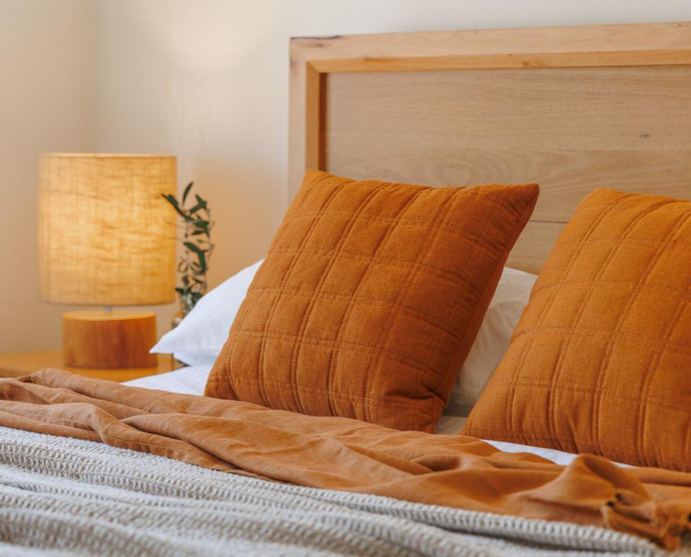 A bed with orange cushions and a warm wooden lamp beside.