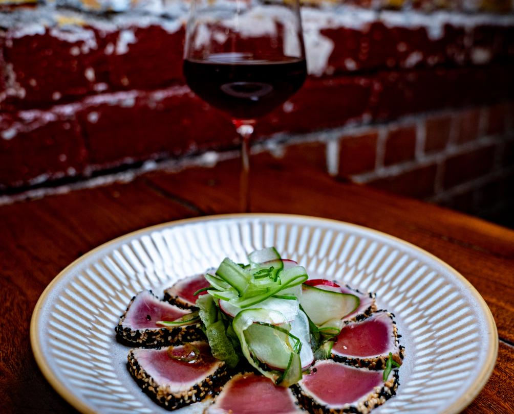 A decadent plate of tuna sashimi served with a glass of red wine.