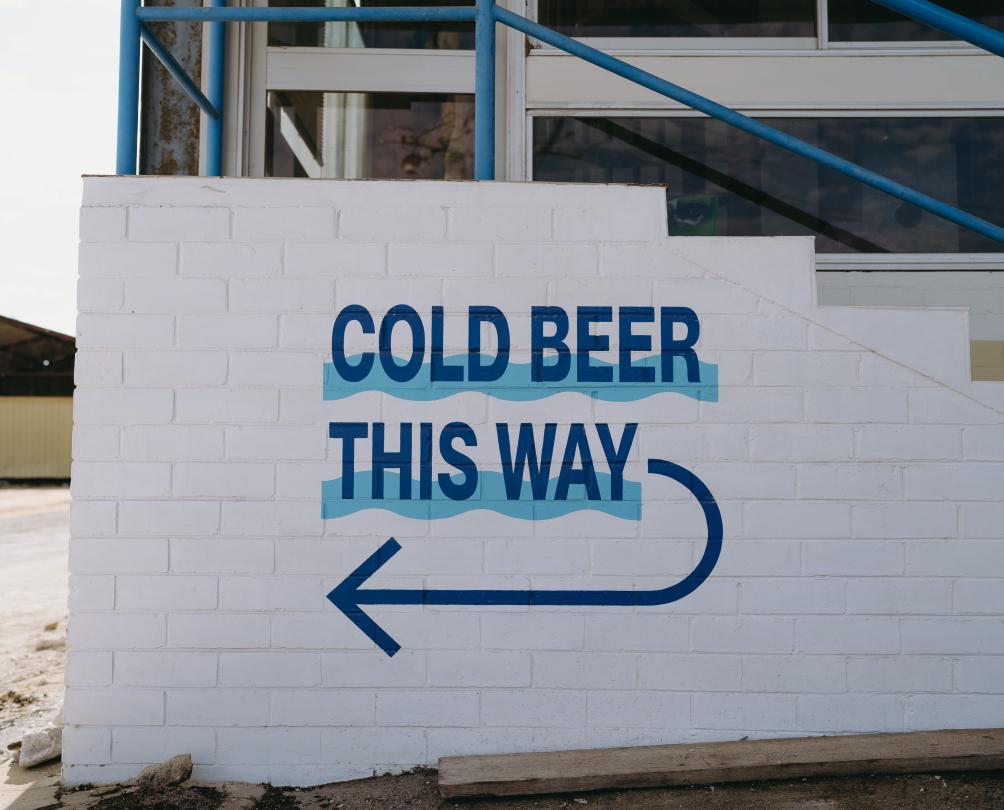 A white washed brick staircase with the words Cold Beer This Way in blue.