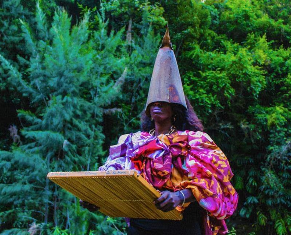 Woman with cone on her head and bright outfit holding a wooden board