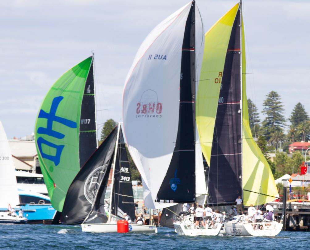 Two sailing boats racing close to each other in front of a harbour.
