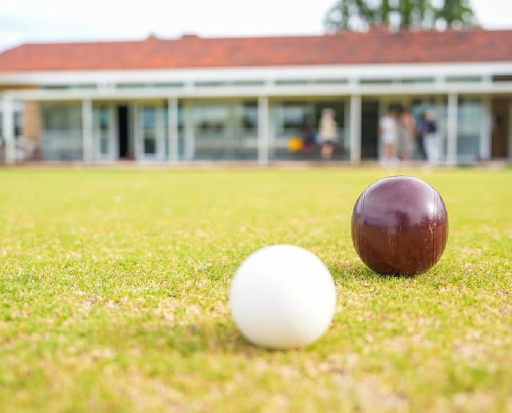 A lawn bowls ball and puck on a green lawn with a clubhouse in the background.