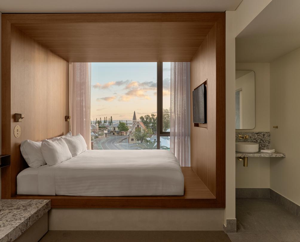 The interior of a hotel room with a floor to ceiling window looking out onto a city.