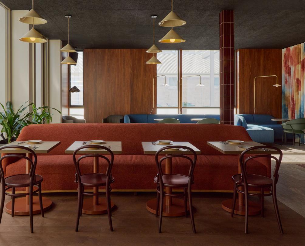 The interior of a restaurant in warm red and orange tones with plush blue and red furniture.
