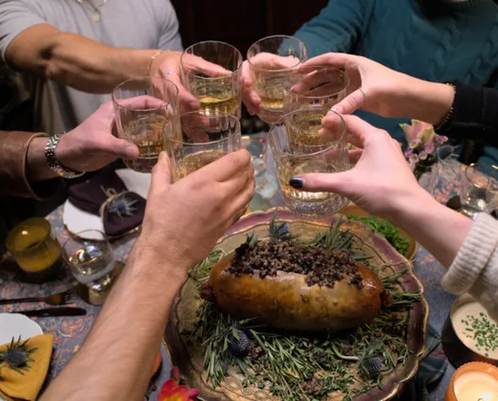 A group of people around a table cheersing drinks together.