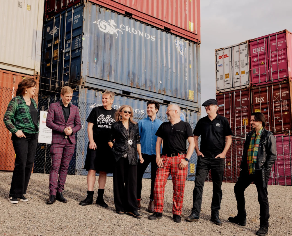 A group of men posing in front of shipping containers, many wearing tartan.