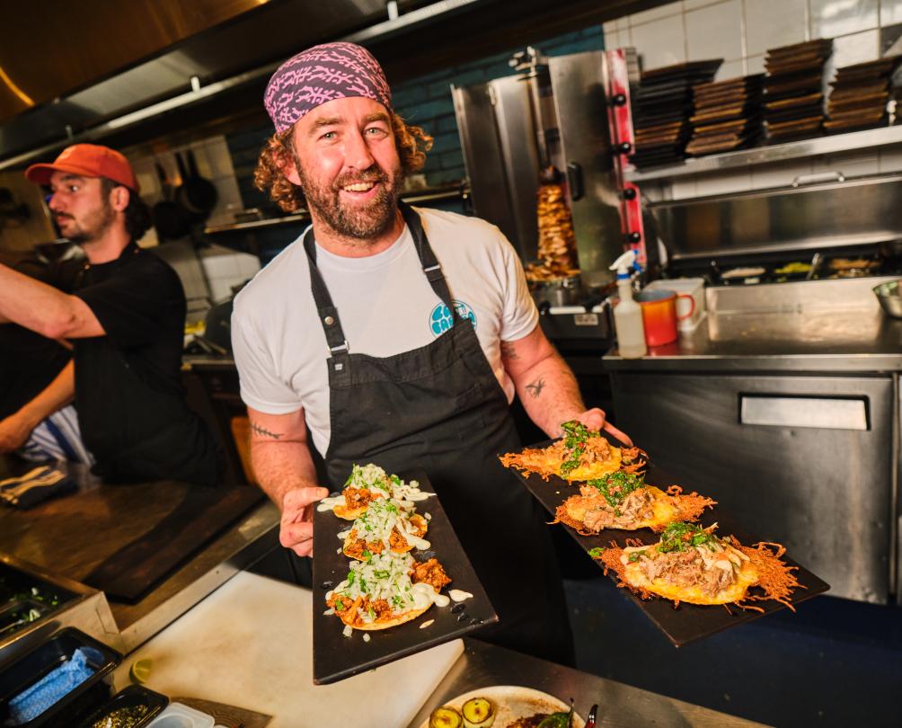 A chef holding two plates full of tacos.